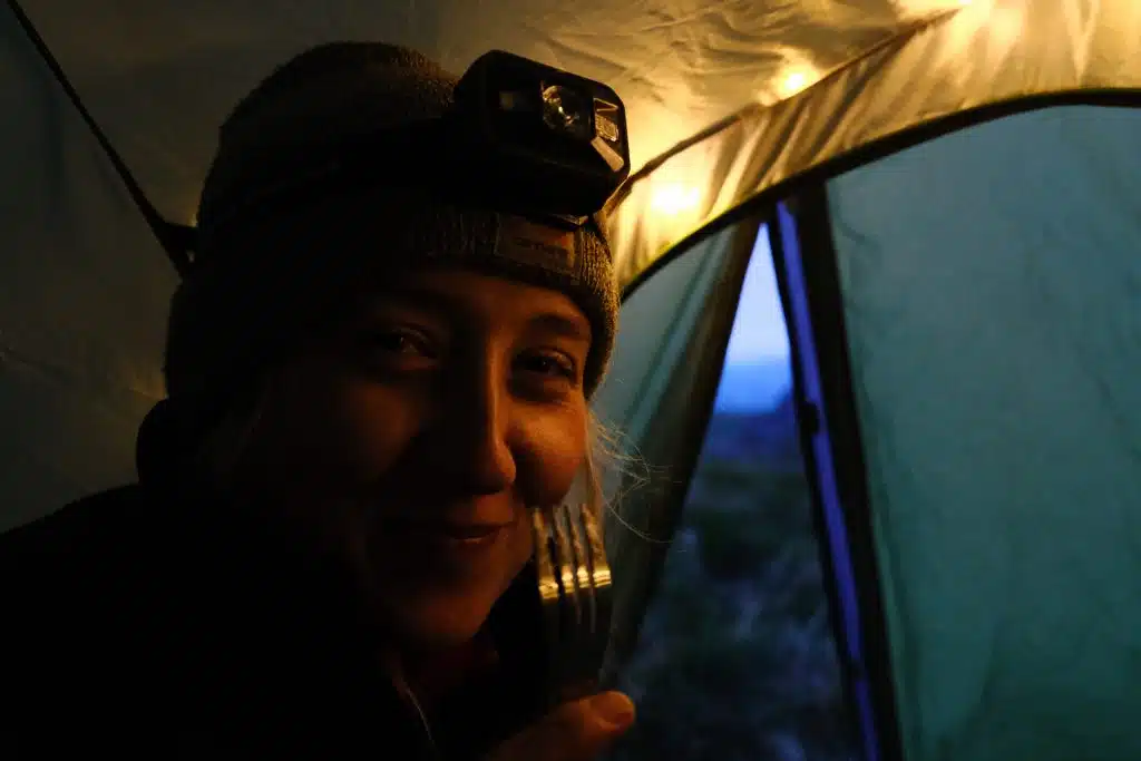 Girl with a headtorch eating a camping meal in tent