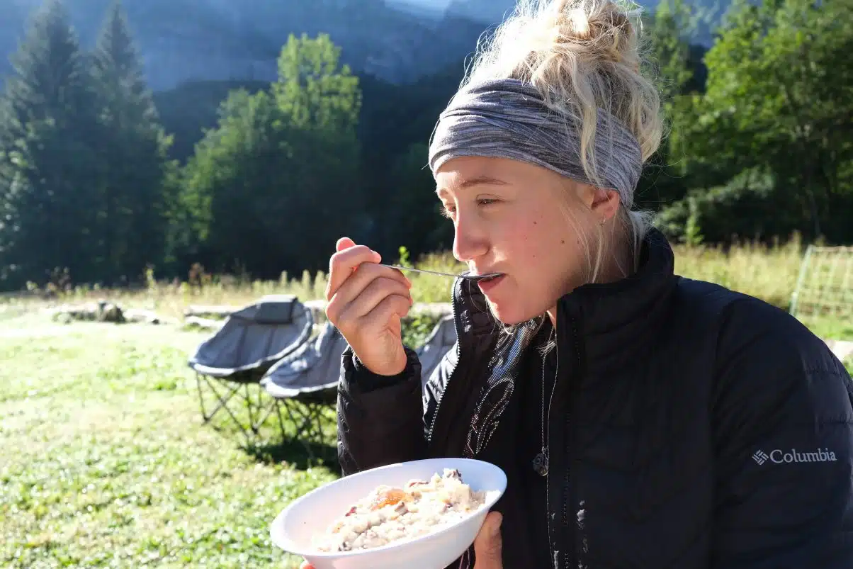 Camping girl eating porridge with vegan coat 