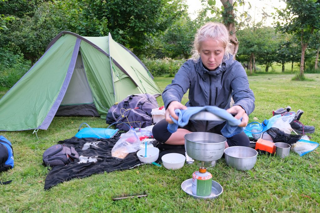 Girl camping in tent and cooking a camping meal on a camping stove