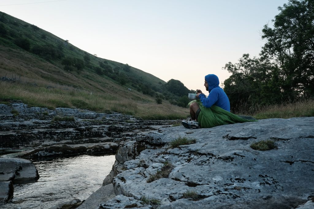 Man on his own adventure sitting by river eating a camping meal